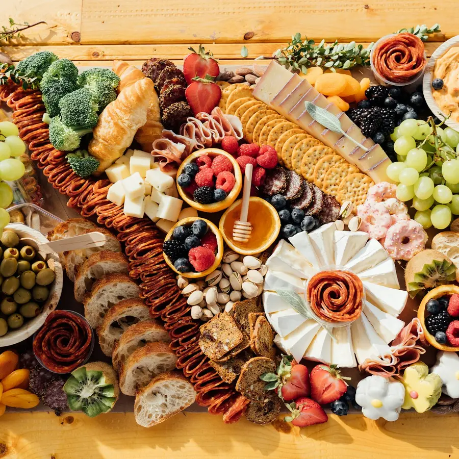 A wooden board with cured meats, cheeses, olives and bread, seen from above