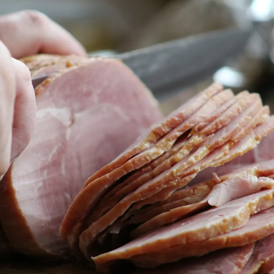 Hands slicing a cooked ham with a long knife