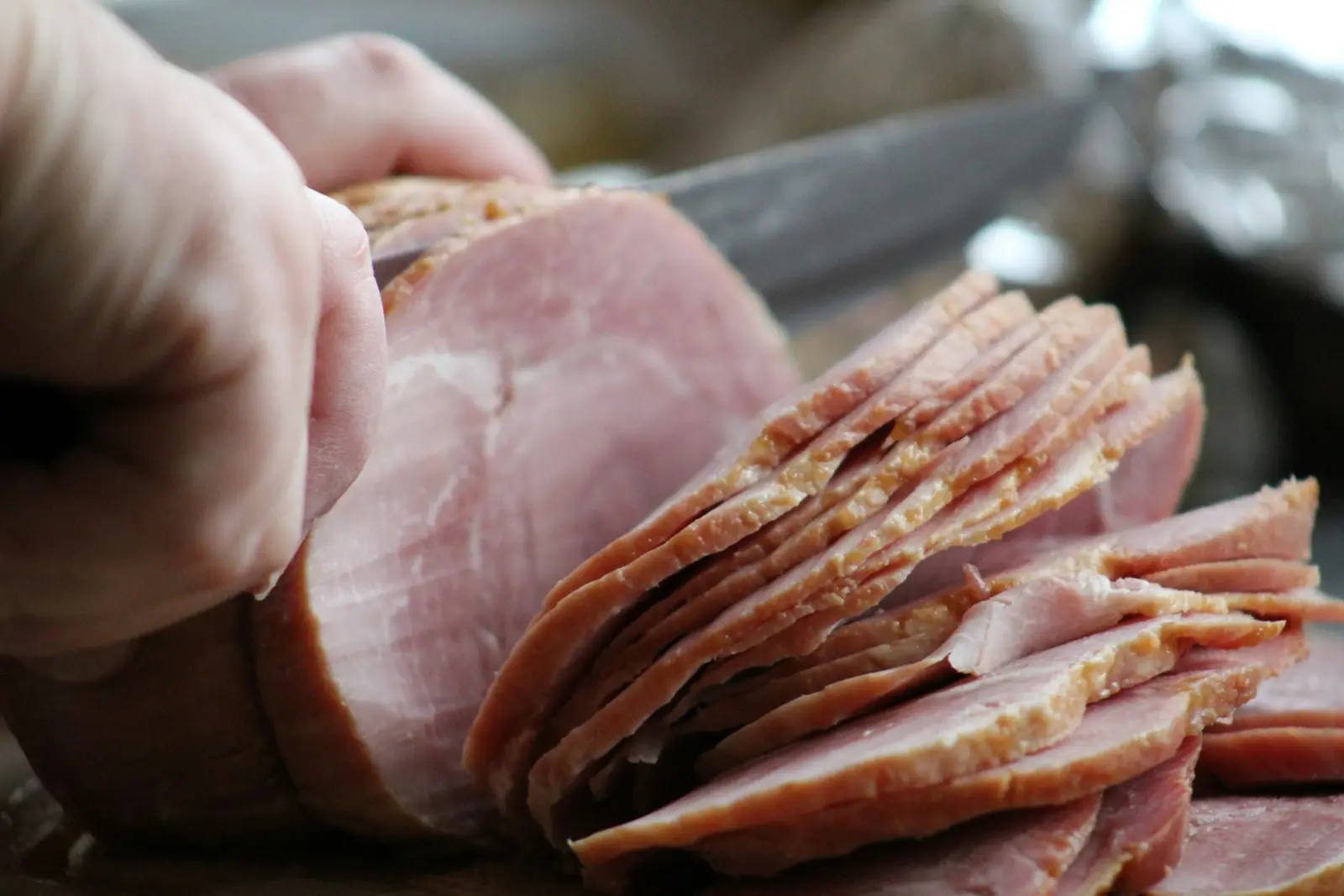 Hands slicing ham with a long knife